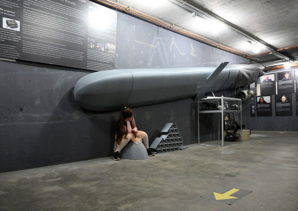 A young visitor sits under the remains of a Russian KH-101 cruise missile during a press presentation of the "Ukraine Museum" in the "Berlin Story Bunker" on February 23, 2026, in Berlin.