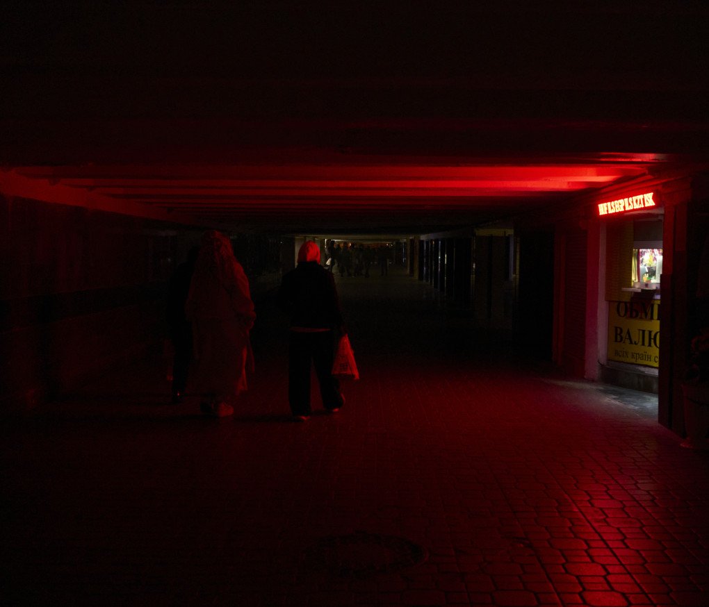 En medio del apagón, una compradora se desplaza por los pasillos subterráneos de Kyiv, iluminados únicamente por una luz roja. 18 de noviembre de 2025. Foto de Joshua Olley/UNITED24 Media.