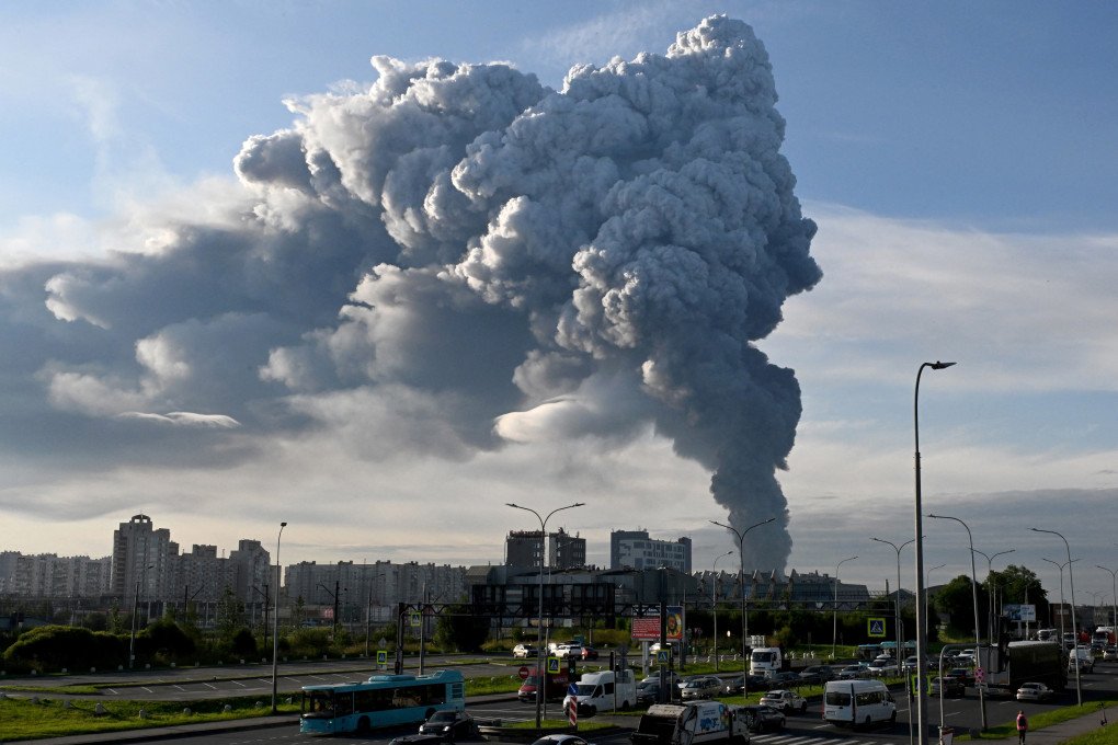 Cars drive along the road as smoke rises above residential buildings from a warehouse for a Russian e-commerce giant near Saint Petersburg after being hit by Ukrainian drones early on July 24, 2026. (Photo by AFP via Getty Images)