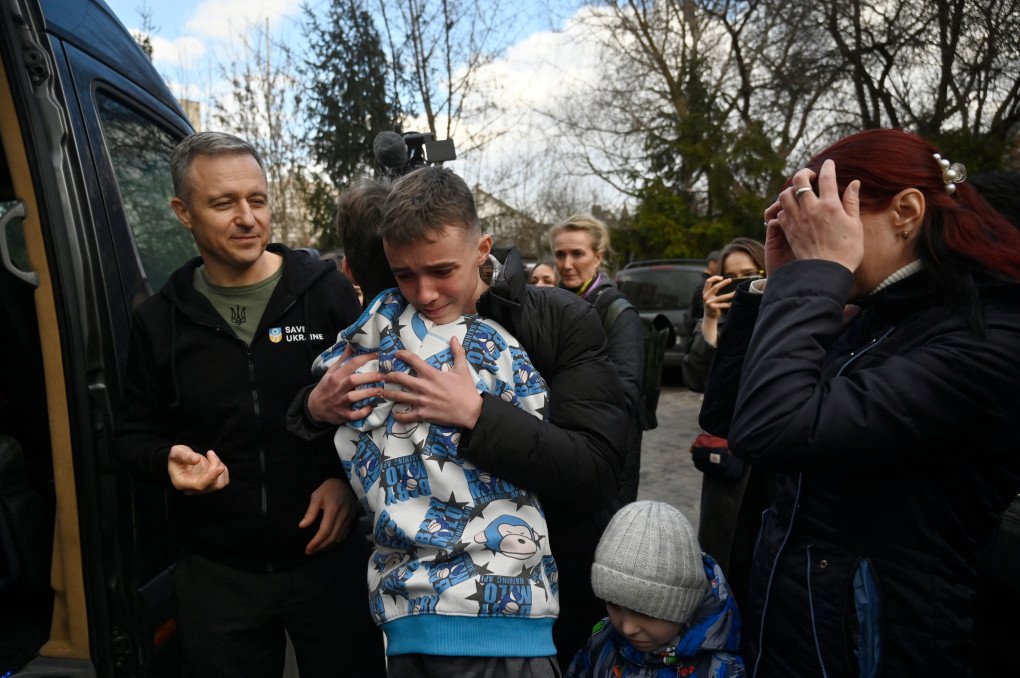 KYIV, UKRAINE - MARCH 22, 2023: Inessa embraces her son, Vitaly, as he steps off the bus that brought him and over a dozen other children back from Russian-occupied territory to Kyiv. Since Russia's full-scale invasion on February 24, 2022, more than 16,000 Ukrainian children have reportedly been deported and forcibly transfered to Russia and Russian-occupied territories, with many sent to institutions or placed in foster care. (Photo by SERGEI CHUZAVKOV / AFP) (Photo by SERGEI CHUZAVKOV/AFP via Getty Images)
