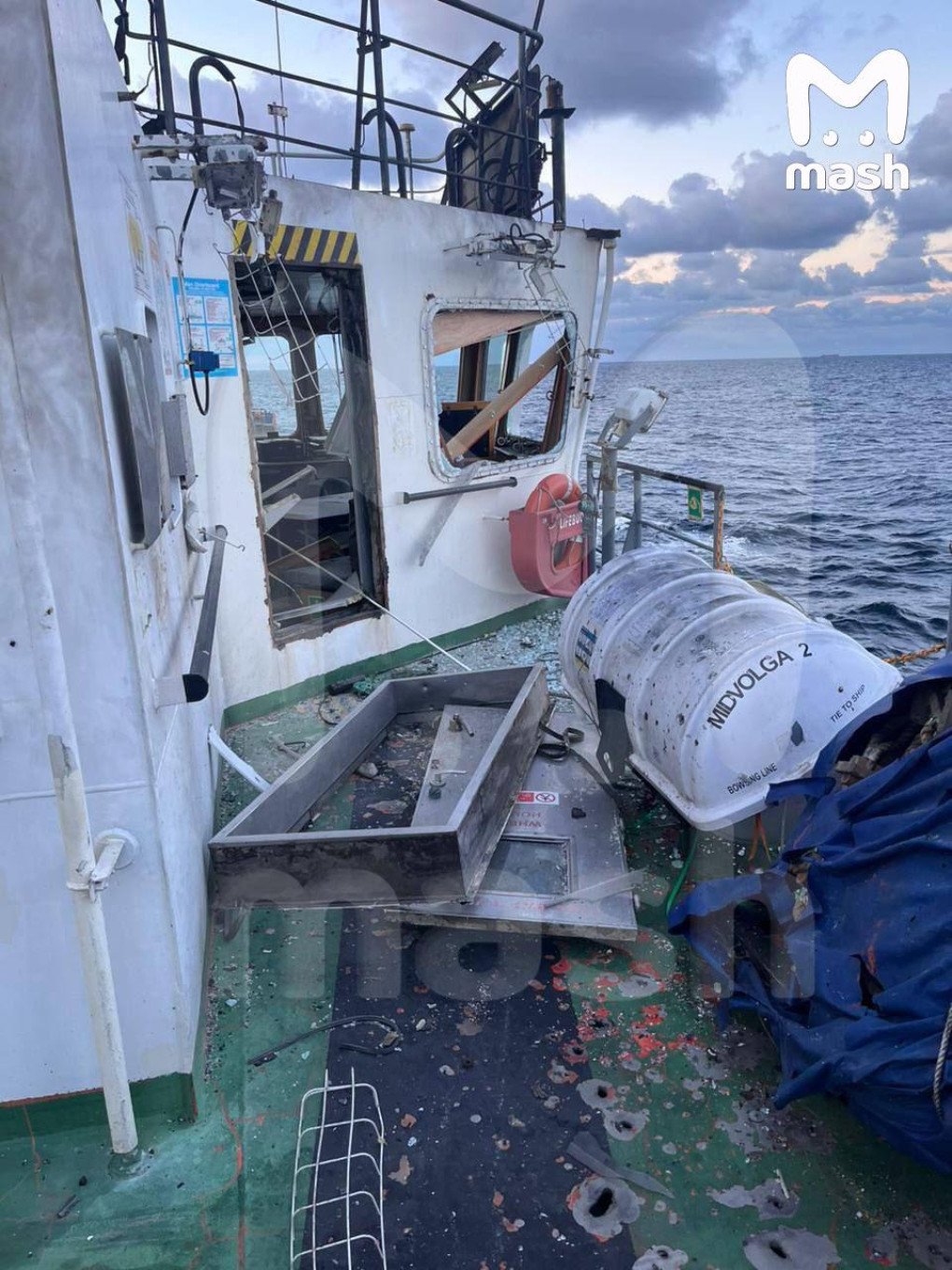 Se muestran ventanas rotas, agujeros de metralla y escombros cerca de un bote salvavidas etiquetado como MIDVOLGA 2, lo que indica daños externos por explosión en el área del puente. (Fuente: Mash) Se muestran ventanas rotas, agujeros de metralla y escombros cerca de un bote salvavidas etiquetado como MIDVOLGA 2, lo que indica daños externos por explosión en el área del puente. (Fuente: Mash)