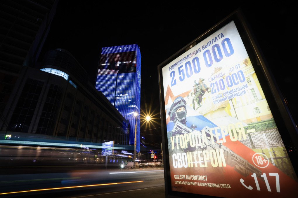 A billboard calling for military service under contract in the ranks of the Russian Armed Forces. Behind, is a multimedia light projection of Putin on the facade of a business center in St. Petersburg, Russia. Photo: Artem Priakhin/SOPA Images/LightRocket via Getty Images