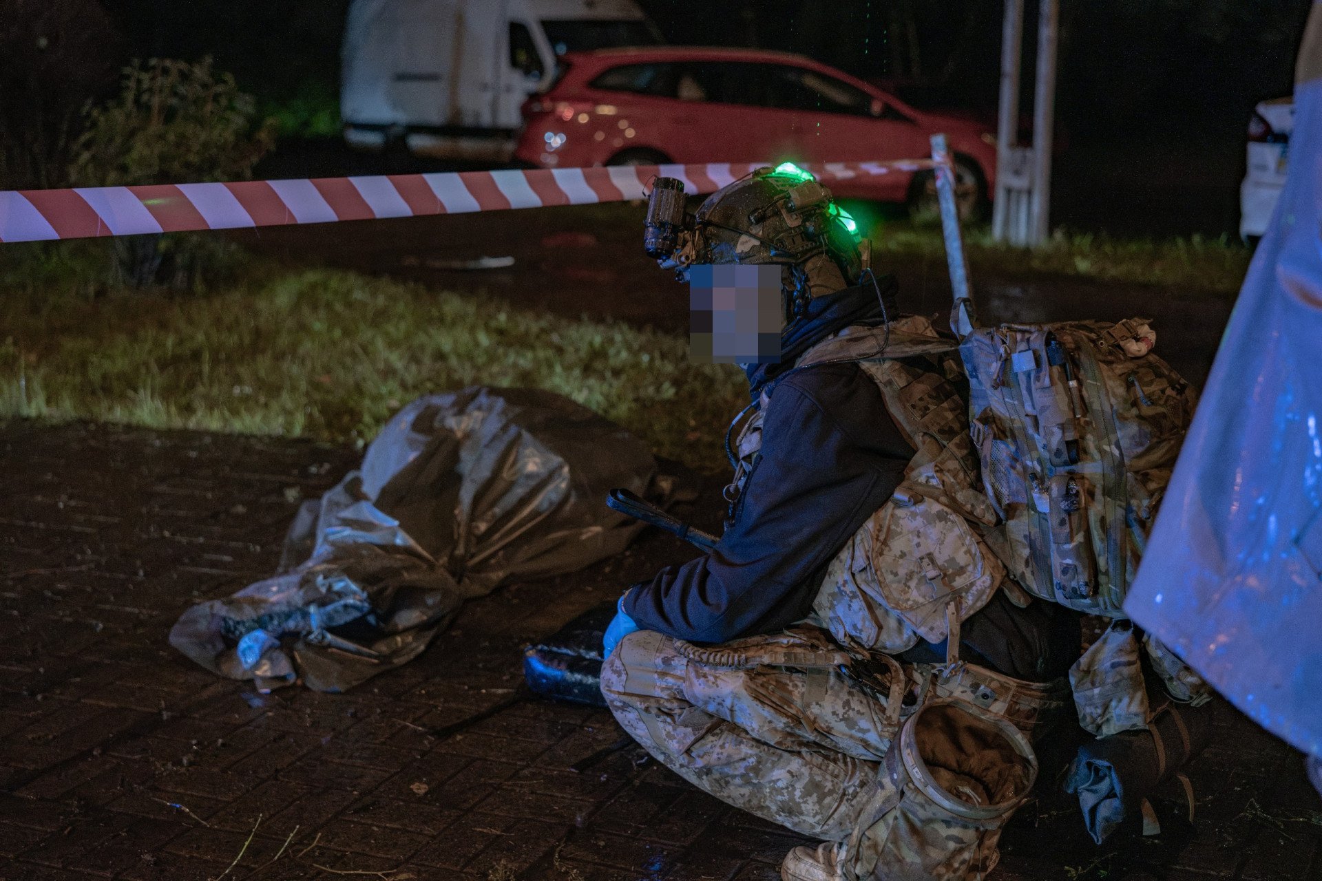 Lastivka, commander of Medical Crew 13, kneels beside the covered body of a civilian victim following a Russian missile strike on Kyiv. Young volunteer paramedics are often among the first on the scene, documenting casualties and providing immediate trauma care amid ongoing aerial attacks. (Photo: Nikita Lisovyi / UNITED24 Media) Medical Crew 13 commander Lastivka kneeling beside a covered civilian victim at a Russian missile strike site in Kyiv.