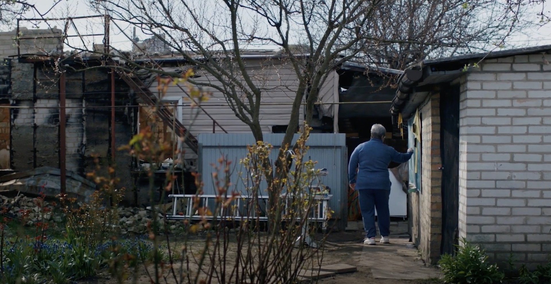 In Borodyanka, a town northwest of Kyiv that was liberated by Ukrainian forces in April 2022 after fierce fighting, a striking scene shows a woman standing in her garden, pointing at a blackboard, seemingly alone. Only in the next scene do we realize a laptop sits before her, with a group of children listening virtually. (Source: 2Brave Productions)