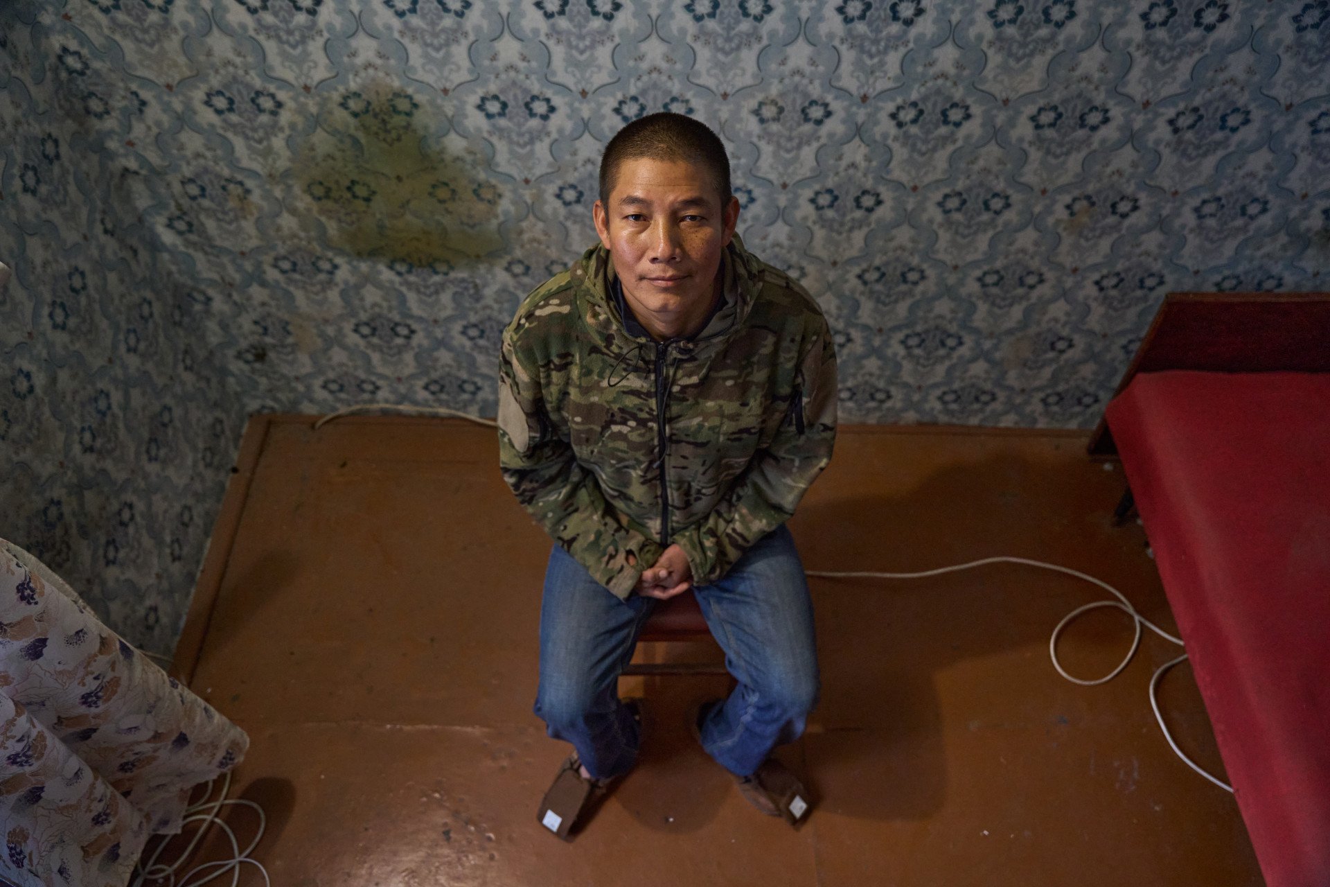 Seated for an interview in Ukraine, Peruvian POW Americo Valdivia Teco looks upward, offering a hopeful grin toward the end of the session. Before the photo was taken, Valdivia Teco expressed deep gratitude for finally being able to speak in his native Spanish after months of being screamed at and ordered around in Russian while serving as a forced conscript on one of the most violent sectors of the frontline during Russia's full-scale invasion of Ukraine. (Photo: Mykyta Shandyba / UNITED24 Media) An overhead shot of Peruvian POW Americo Valdivia Teco looking up with a slight smile during an interview in Ukraine, after months of serving as a forced conscript on Russia's frontlines.