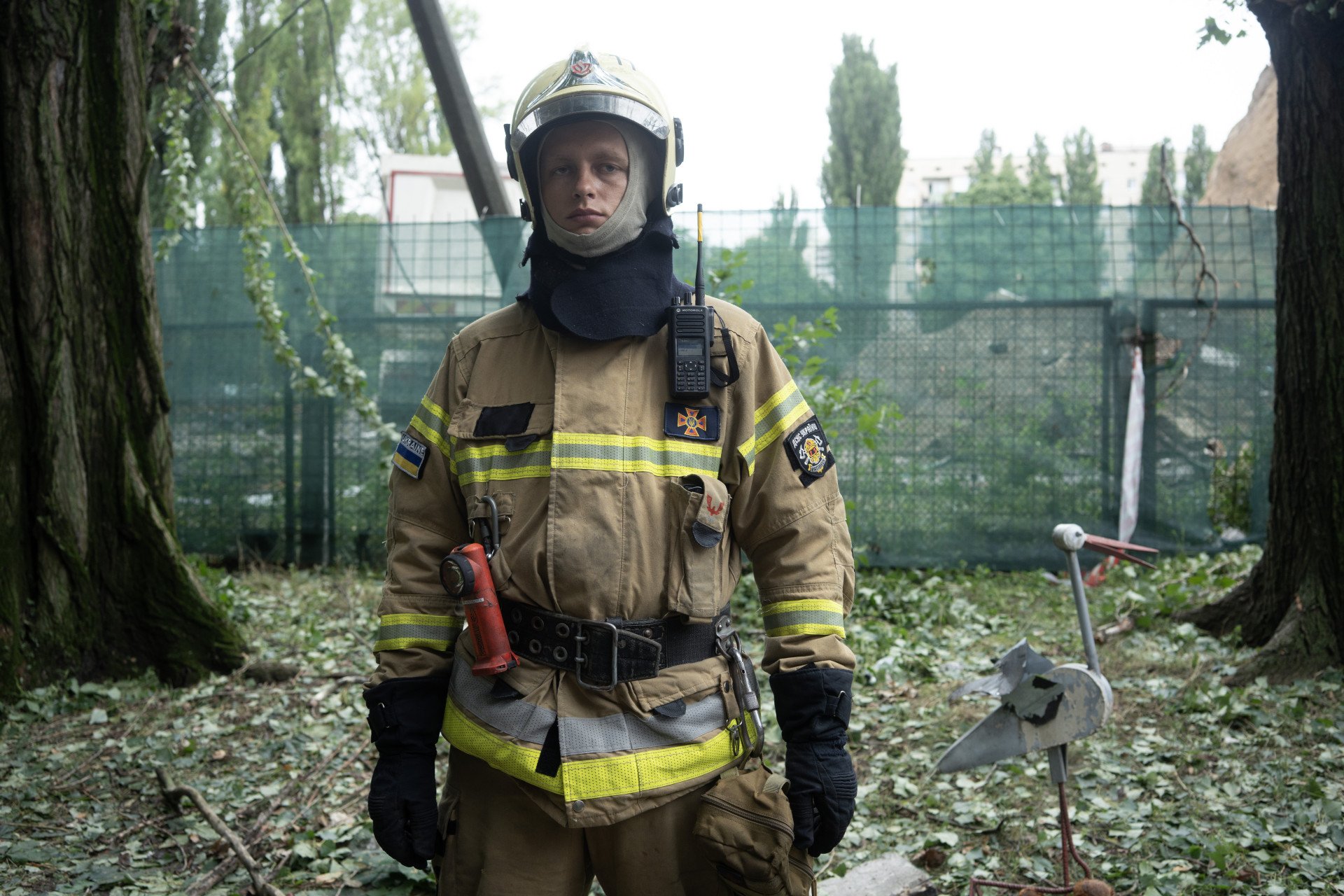 A Ukrainian firefighter stands in front of a children’s metal sculpture,  one of the few things left intact in a neighborhood shattered by a Russian missile strike. Kyiv, Ukraine. July 31, 2025. Photo by Josh Olley/UNITED24 Media