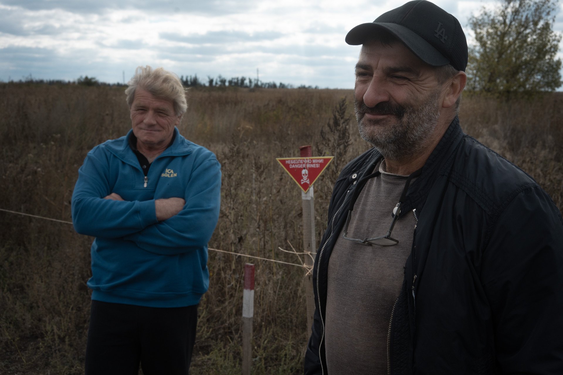 Valerii, overlooking his fields now marred by mines, standing next to his brother, Yurii. Dovhenke, Ukraine. October, 2025. Photo by Joshua Olley/UNITED24 Media.