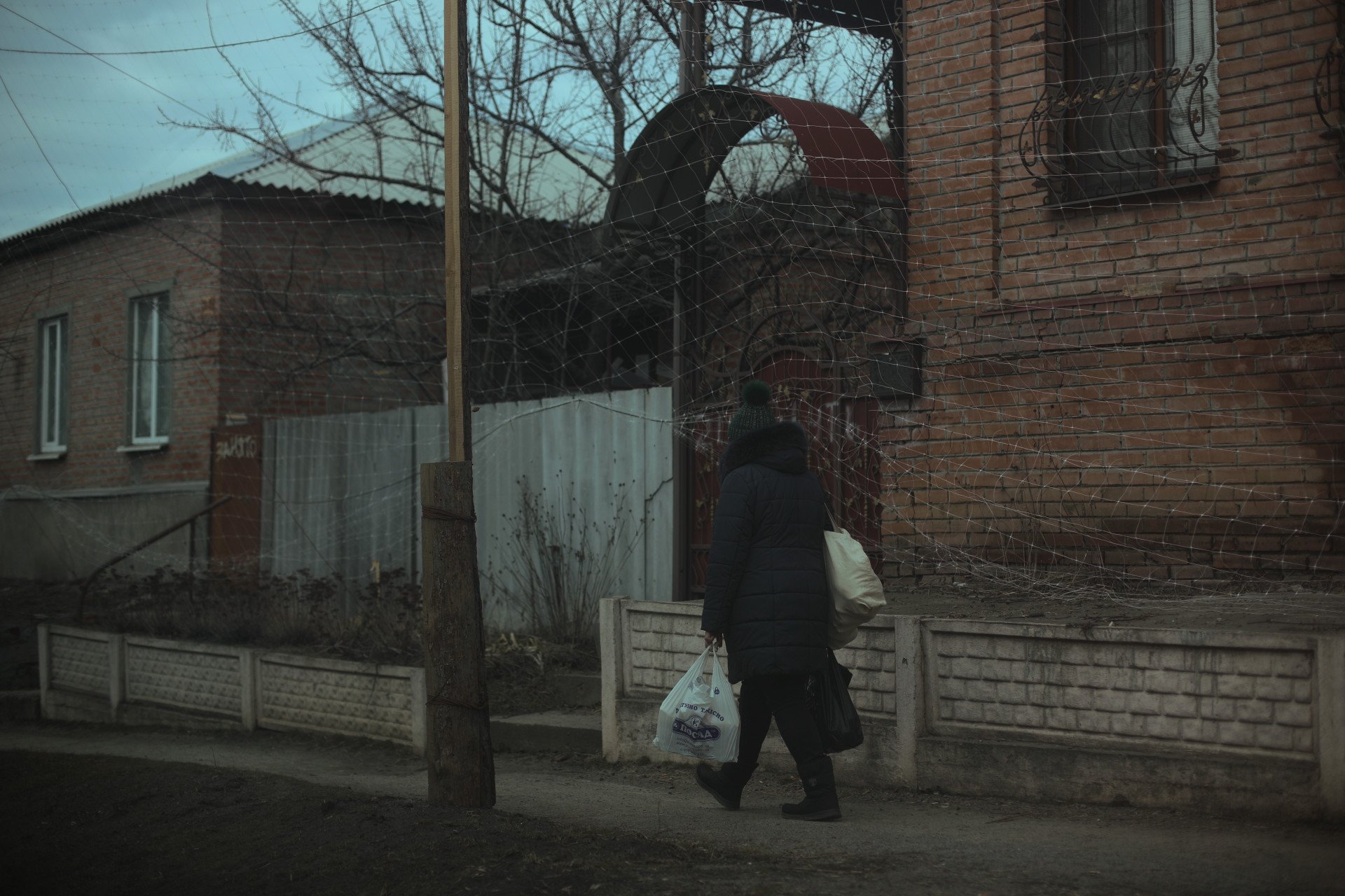 Un residente de Izium camina por una calle cubierta con redes antidrones, cargando víveres a principios de marzo de 2026. (Foto: Lucile Brizard/UNITED24 Media) Un residente de Izium camina por una calle cubierta de redes anti-drone.