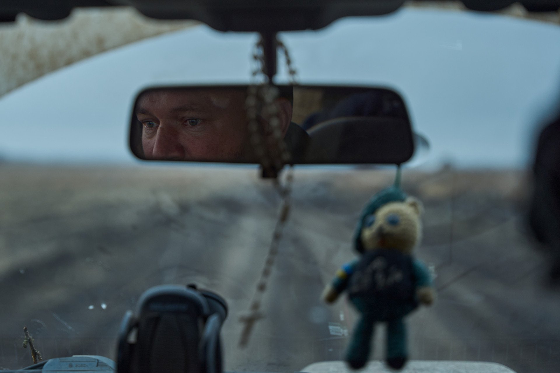 The senior artillery technician scans the road and sky en route to the firing position, his protective charm swaying from the mirror. (Photo: Mykyta Shandyba)