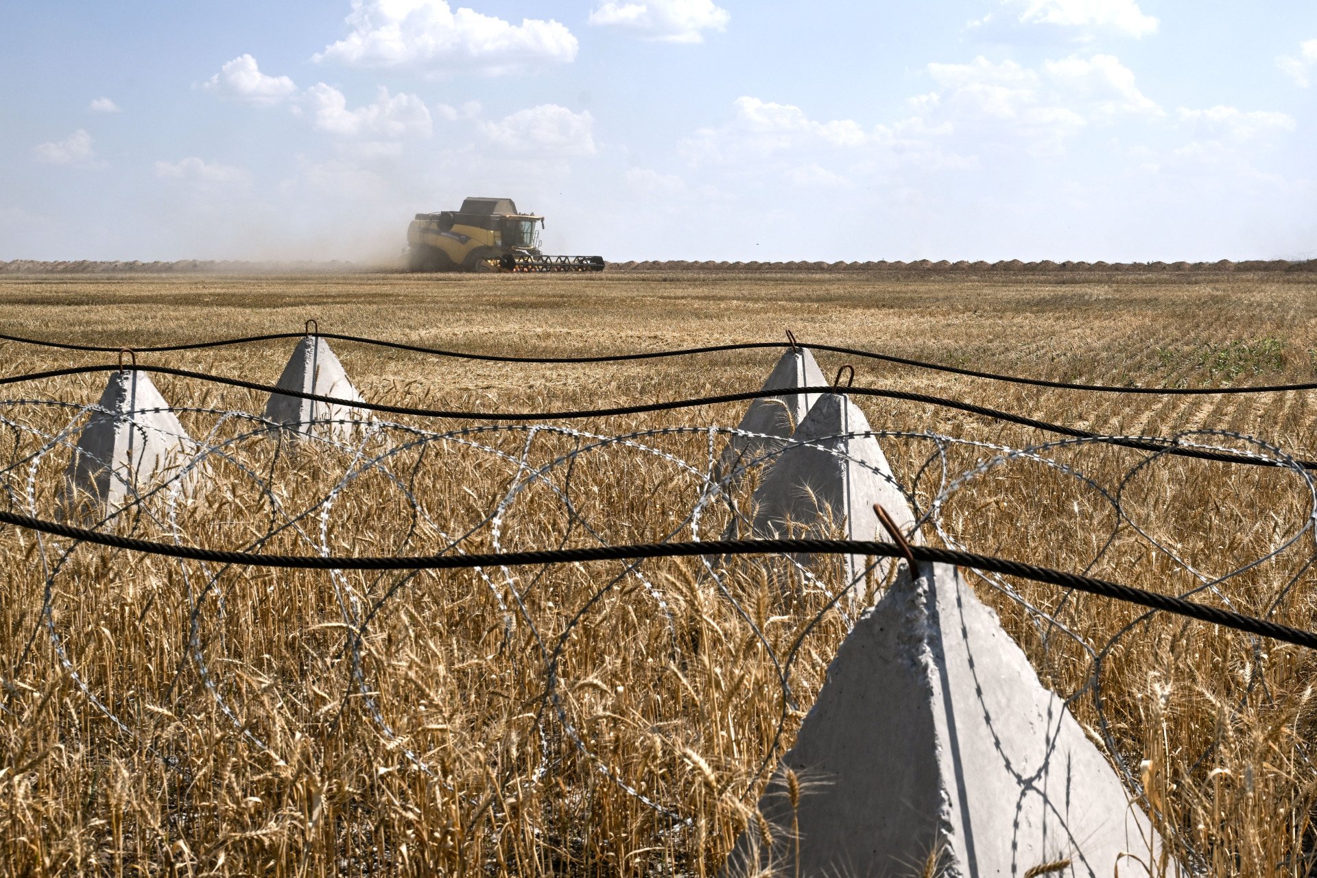 A combine harvester collects grain crops along pyramidal anti-tank obstacles and barbed wire in a field near Orikhiv, Zaporizhzhia region, Ukraine, on July 8, 2025. (Source: Getty Images) A combine harvester collects grain crops along pyramidal anti-tank obstacles and barbed wire in a field near Orikhiv, Zaporizhzhia region, Ukraine, on July 8, 2025. (Source: Getty Images)
