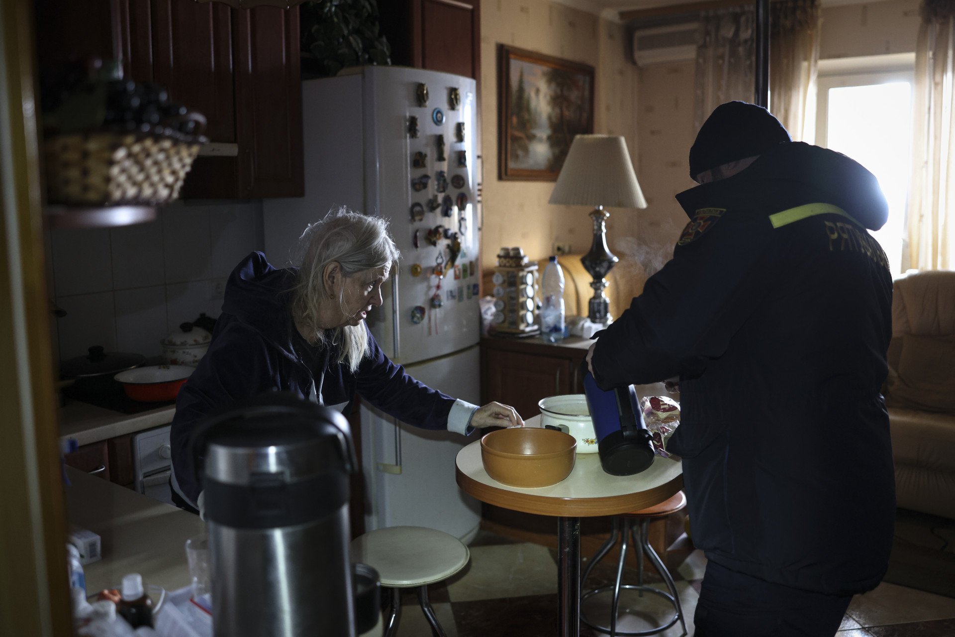 National Guard and State Emergency Service workers deliver water and food to Tetiana Yelinson, an elderly resident of Kyiv’s Troieshchyna district, on Jan. 14, 2026, after Russian strikes on critical infrastructure left parts of the capital without heating and water. Nearby, residents warm themselves and charge mobile phones in a heated tent as temperatures in unheated buildings dropped amid severe frosts. (Photo: Getty Images)