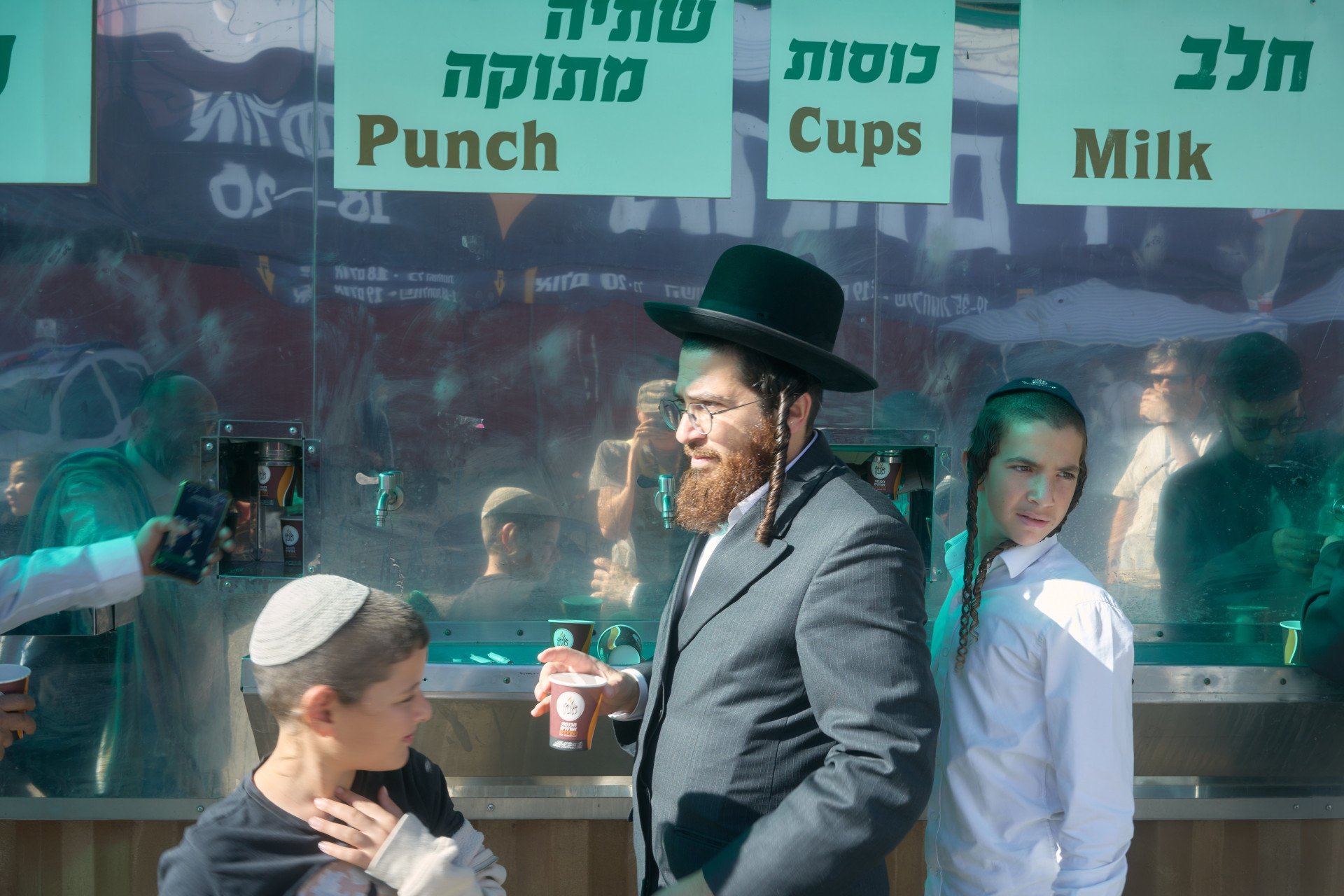 Father and his two sons get coffee and the free coffee dispenser. A lot of the food and coffee is free. Many pilgrims, local residents, and especially large Jewish organizations set up community kitchens and tents offering meals, drinks, and snacks at no cost. Uman, Ukraine. September, 2025. Photo: Josh Olley/UNITED24 Media