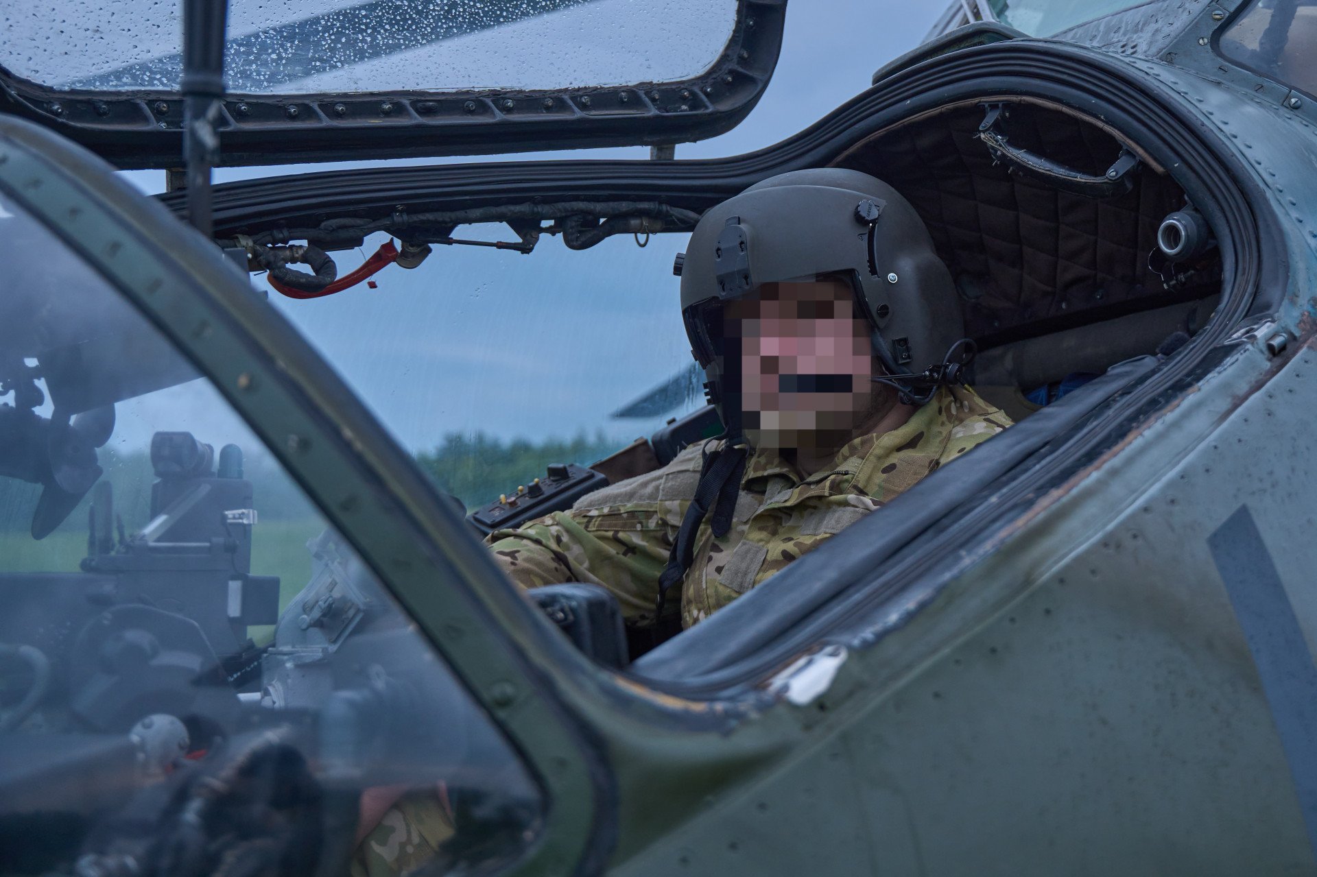 A Ukrainian pilot Andrii in full gear sits inside the cockpit of a Mi-24 helicopter, ready for deployment under overcast skies. A Ukrainian pilot Andrii in full gear sits inside the cockpit of a Mi-24 helicopter, ready for deployment under overcast skies.