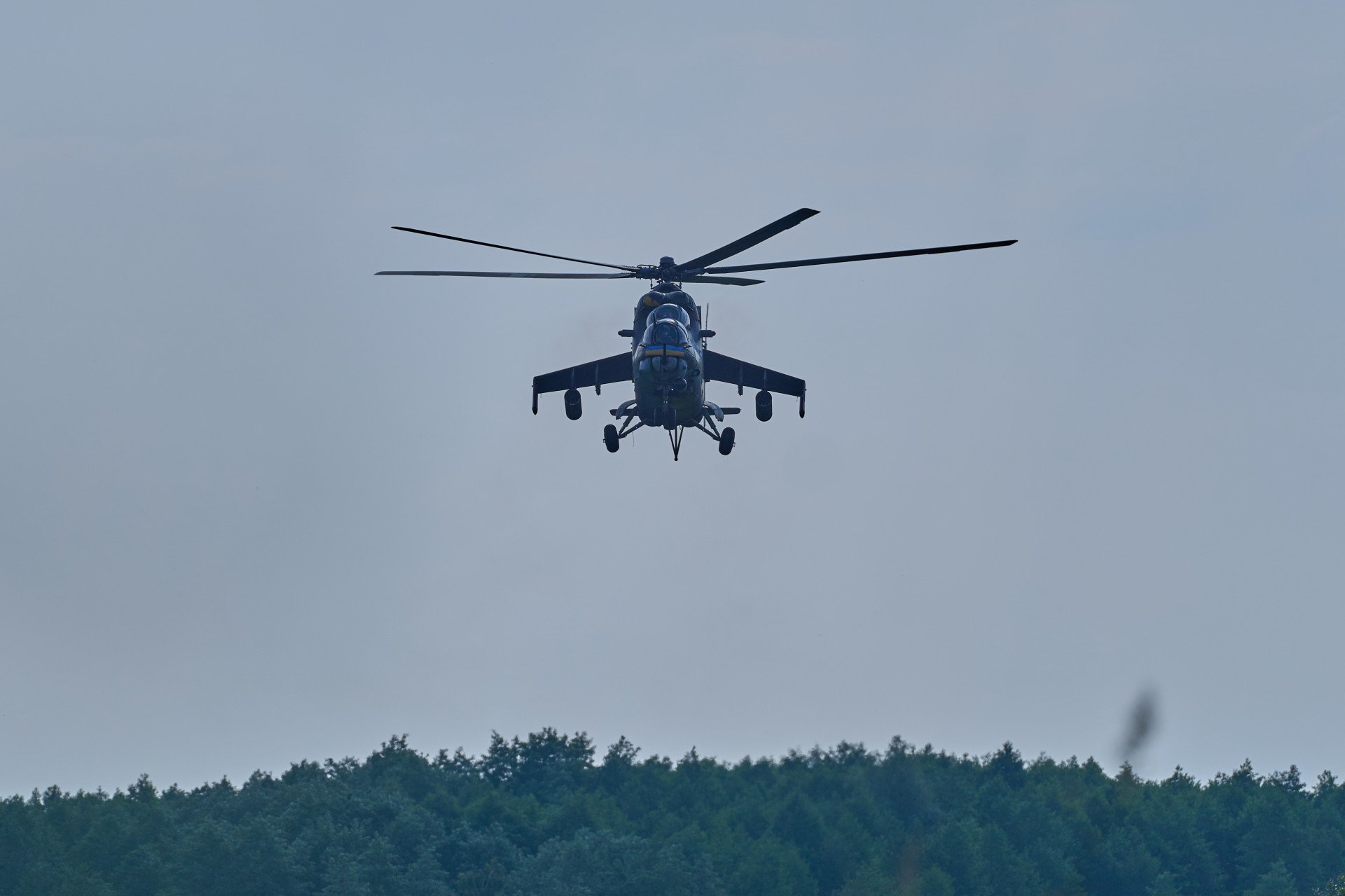 A Ukrainian Mi-24 helicopter ascends over the treetops, heading out on a combat mission under overcast skies. A Ukrainian Mi-24 helicopter ascends over the treetops, heading out on a combat mission under overcast skies.