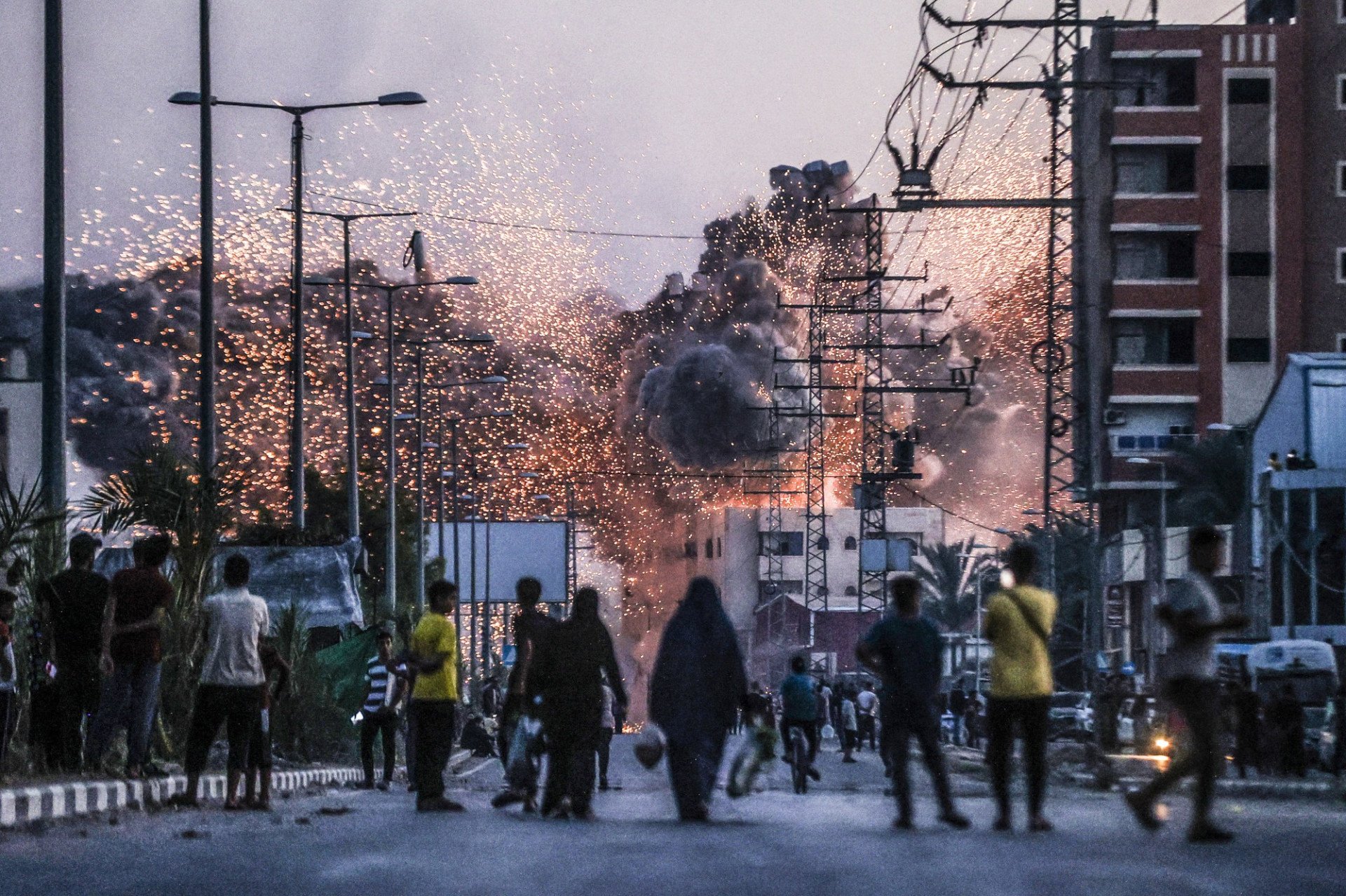 Palestinians stand on a road as black smoke and flames rise above a building following Israeli attacks in Deir al-Balah, Gaza, on June 6, 2024. (Photo: Ali Jadallah / Anadolu Agency)