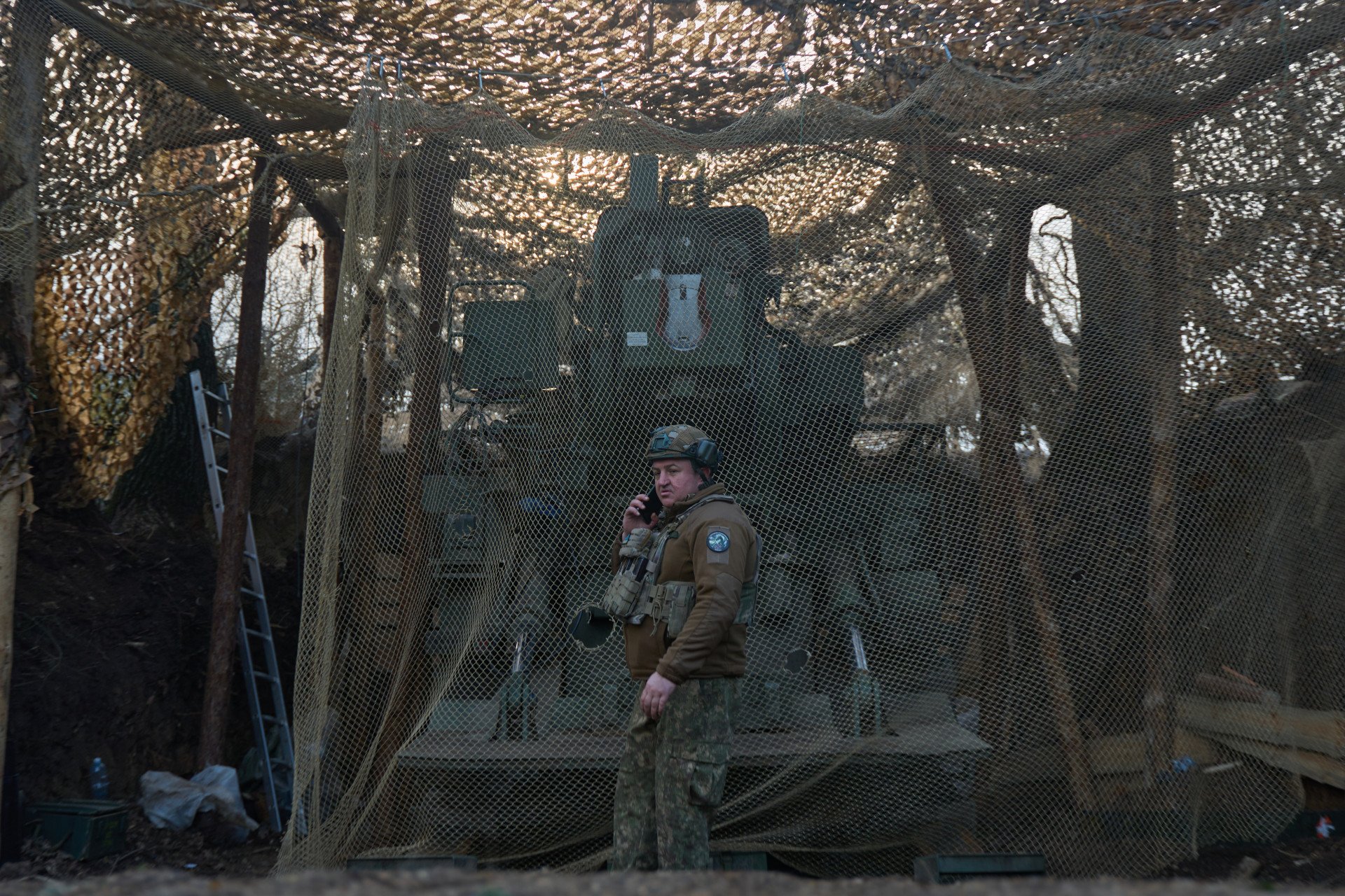 A Ukrainian artilleryman communicates by radio in front of the Bohdana self-propelled artillery system, camouflaged under netting at a frontline position. A Ukrainian artilleryman communicates by radio in front of the Bohdana self-propelled artillery system, camouflaged under netting at a frontline position.