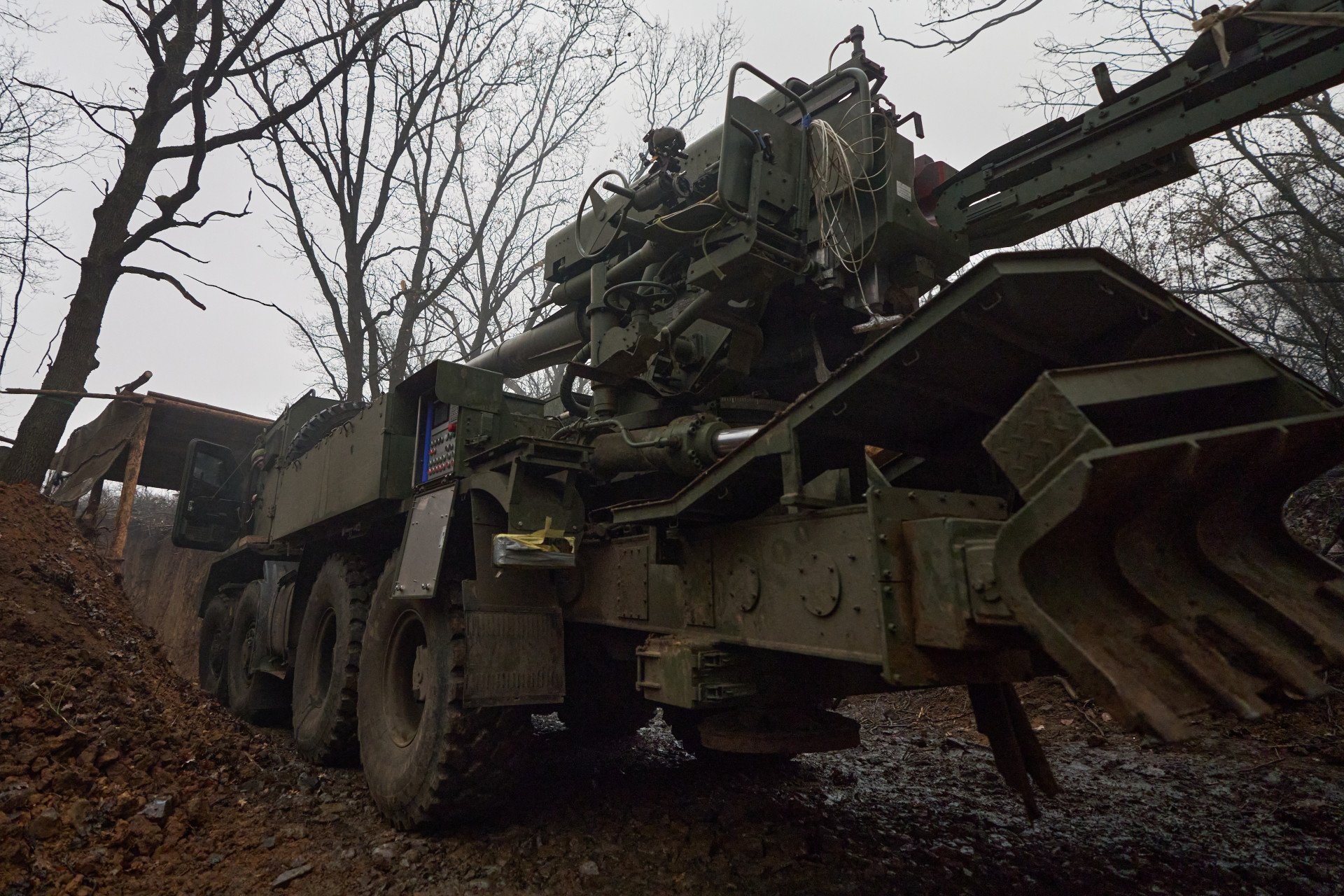 The howitzer moves from one dugout to another to shoot at Russian positions. The Bohdana only moves back and forth here to avoid being spotted. The winter rain soaks the soil, making it muddy, slippery, and challenging to move such a humongous cannon out of its position. Here, the cannon is mounted on an 8-wheeled chassis truck, adapted with claws at the back to ground the howitzer, whose recoil is massive. 