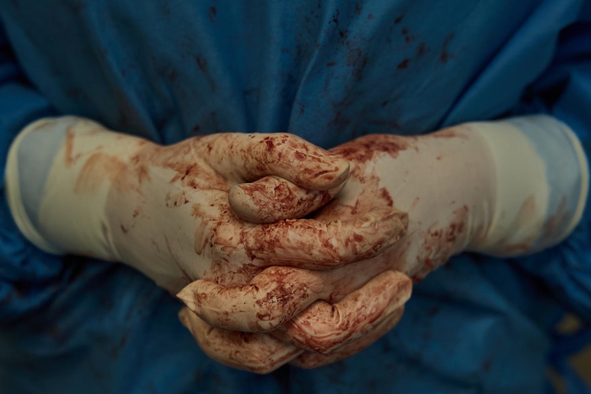 Clasped together in a rare moment of stillness, these blood-stained hands tell the raw story of a grueling battle against time. Every line on these surgical gloves represents hours of intense focus, immense physical strain, and a profound responsibility. In a rare quiet moment during a cardiac transplant, this striking image serves as a powerful testament to the resilience of Ukraine's medical heroes. (Photo: Mykyta Shandyba / UNITED24 Media) Close-up of a surgeon’s blood-stained gloved hands clasped together after a heart transplant operation.