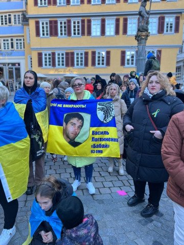 Maryna holding a Ukrainian flag featuring a photo of Vasyl and the words "Heroes never die." (Source: Maryna's personal archive)