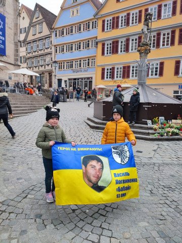 Myroslav and Solomiia holding a Ukrainian flag featuring a photo of Vasyl and the words "Heroes never die." (Source: Maryna's personal archive)