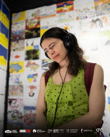 Un visitante escucha un audiolibro en la exposición, de pie frente a una pared llena de dibujos infantiles realizados durante la guerra. (Fuente: Bring Kids Back UA)