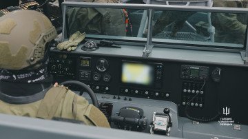 A Ukrainian military intelligence service member sits at the helm of a newly delivered armed patrol boat, with navigation and communications equipment visible at the control console. (Source: HUR)