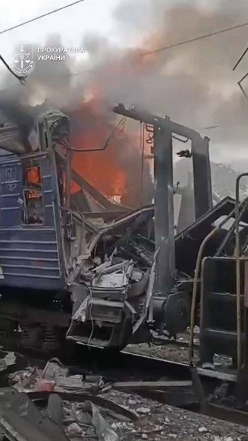 Close-up of the destroyed passenger carriage in Shostka. Flames engulf the interior as Ukrainian prosecutors document the aftermath of the strike. (Source: Andrii Sybiha)