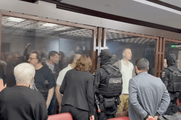 Defendants shout their innocence from behind a glass enclosure as armed security forces stand guard during court hearing in Rostov-on-Don, Russia. (Source: Medizona)