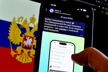 The MAX app logo is displayed on a mobile phone screen in front of a Russian flag as a person uses the application in Moscow, Russia. (Source: Getty Images)