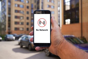 Man holding a smartphone displaying a “No Network” message in a residential area. (Source: Getty Images)