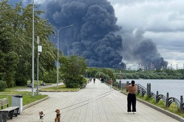 People walk in a park as black smoke rises from the area of the Russian oil producer Gazprom Neft’s Moscow oil refinery on the south-eastern outskirts of Moscow on June 18, 2026. (Source: Getty Images)