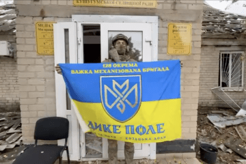 A Ukrainian soldier holds the flag of the 128th Separate Heavy Mechanized Brigade outside a damaged building in Malokaterynivka, Zaporizhzhia region, Ukraine, October 18, 2026.