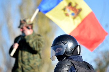 Moldova Warns Its Citizens in Russia of Risk of Being Drafted Under New Military Law A man holds Moldovan national flag as a special police officer patrols a street near a polling station during the second round of Moldova's presidential election in the town of Varnita at Moldova on November 15, 2020. (Source: Getty Images)