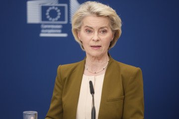 Primer plano de la bandera de la Unión Europea ondeando junto a un monitor que muestra gráficos financieros y fluctuaciones del mercado de criptomonedas