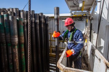 A worker guides drilling pipes from the tower at the Gazprom PJSC gas drilling rig in the Kovyktinskoye gas field. (Source: Getty Images)