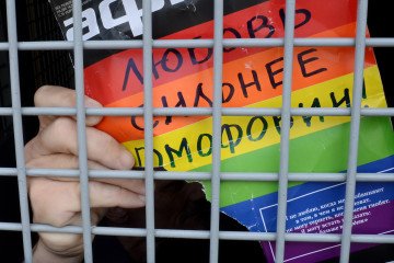 A Russian gay and LGBT rights activist shows a sign reading "Love is stronger than homophobia" from inside a Russian riot police van during an unauthorized gay rights activists rally in central Moscow on May 25, 2013.(Source: Getty Images)