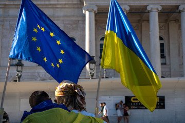A person with a Ukrainian flag and another with the European flag are seen during a gathering in downtown Lisbon, Portugal to protest against the ongoing Russian invasion of Ukraine. (Source: Getty Images)