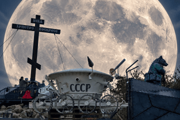 A Soviet-themed lunar rover display marked “USSR” stands beneath a large Orthodox cross in Izborsk, Russia, with the Moon added in the background. (Source: UNITED24 Media)
