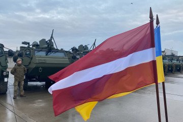 A Latvian and Ukrainian flag wave in front of the vehicles during the handover of 21 Patria 6x6 armored transport vehicles to the Ukrainian armed forces at the Latvian military base in Adazi on November 6, 2025. (Source: Getty Images)