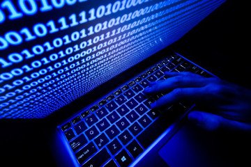 A hand on the keyboard is seen with binary code displayed on a laptop screen. Illustrative image. (Source: Getty Images)
