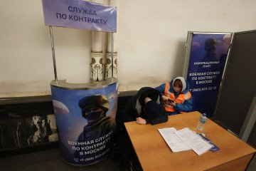 Military enlistment office employees rest near a propaganda stand urging citizens to sign a contract with the Ministry of Defense and go to war with Ukraine, installed in a Moscow metro underpass, on February 16, 2026. (Source: Getty Images)
