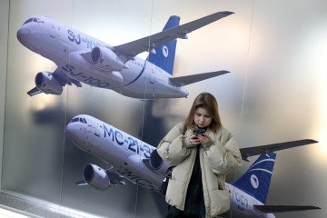 A woman stands next to a banner depicting Russian civil aviation aircraft MS 21-300 and Tupolev TU-214 during the National Aviation Infrastructure Salon (NAIS) on February 4, 2026, in Krasnogorsk, Russia. (Source: Getty Images)