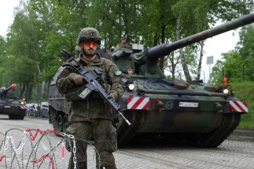 A member of the Homeland Protection Division stands at a checkpoint as PzH 2000 self-propelled howitzers of the 37th Armoured Infantry Brigade deploy during the large-scale exercises on May 20, 2026, near Bergen, Germany.