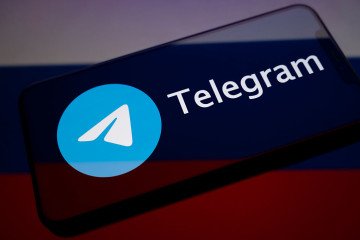 The Telegram logo displays on the screen of a smartphone placed on a reflective surface onto which the Russian flag projects. (Source: Getty Images)