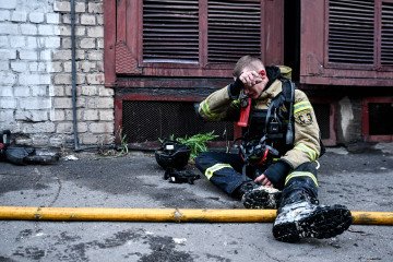 A firefighter wipes his forehead while sitting on the ground during a response effort to a Russian drone attack on June 14, 2025. Illustrative photo.