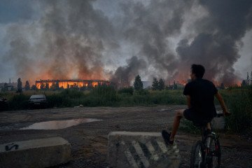 A teenager sits on a bicycle watching flames rise from a burning logistics warehouse following a Russian ballistic missile attack on Kyiv and the surrounding region on August 5, 2026, in Kyiv, Ukraine. A teenager sits on a bicycle watching flames rise from a burning logistics warehouse following a Russian ballistic missile attack on Kyiv and the surrounding region on August 5, 2026, in Kyiv, Ukraine.