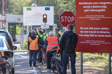 People with bicycles stand at the border between Lithuania and Belarus on August 12, 2023 next to a sign reading "Do not risk your safety -- do not travel to Belarus. You may fail to come back". (Source: Getty Images)