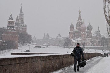 A man walks along a bridge over the Moskva River in central Moscow, with the Kremlin’s Spasskaya Tower and St. Basil’s Cathedral visible in the background on a snowy day, February 12, 2026. (Source: Getty Images)