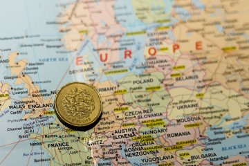 A one-pound coin from the United Kingdom placed over the map of Europe.