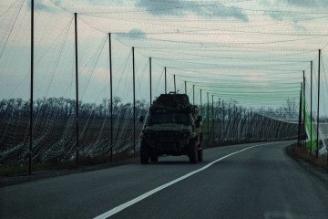 Vehículo blindado ucraniano circulando por carretera protegida con redes anti-drones cerca del frente en el este de Ucrania